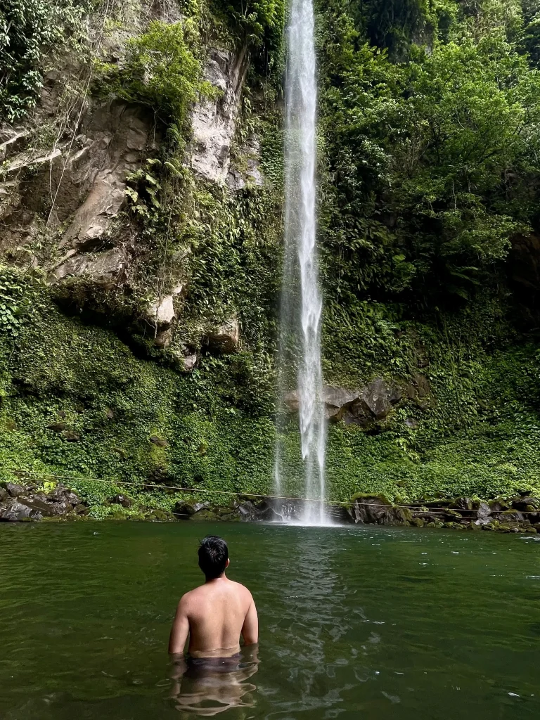 Shirtless man behind his back looking up to Katibawasan Falls