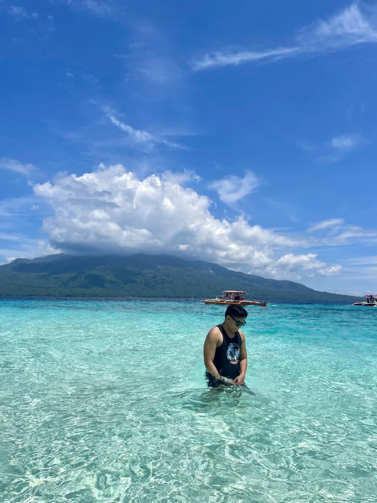 Man posing in the blue water of Mantigue Island with Mount Hibok-Hibok behind