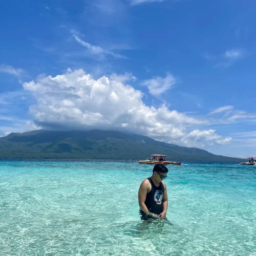 Man posing in the blue water of Mantigue Island with Mount Hibok-Hibok behind